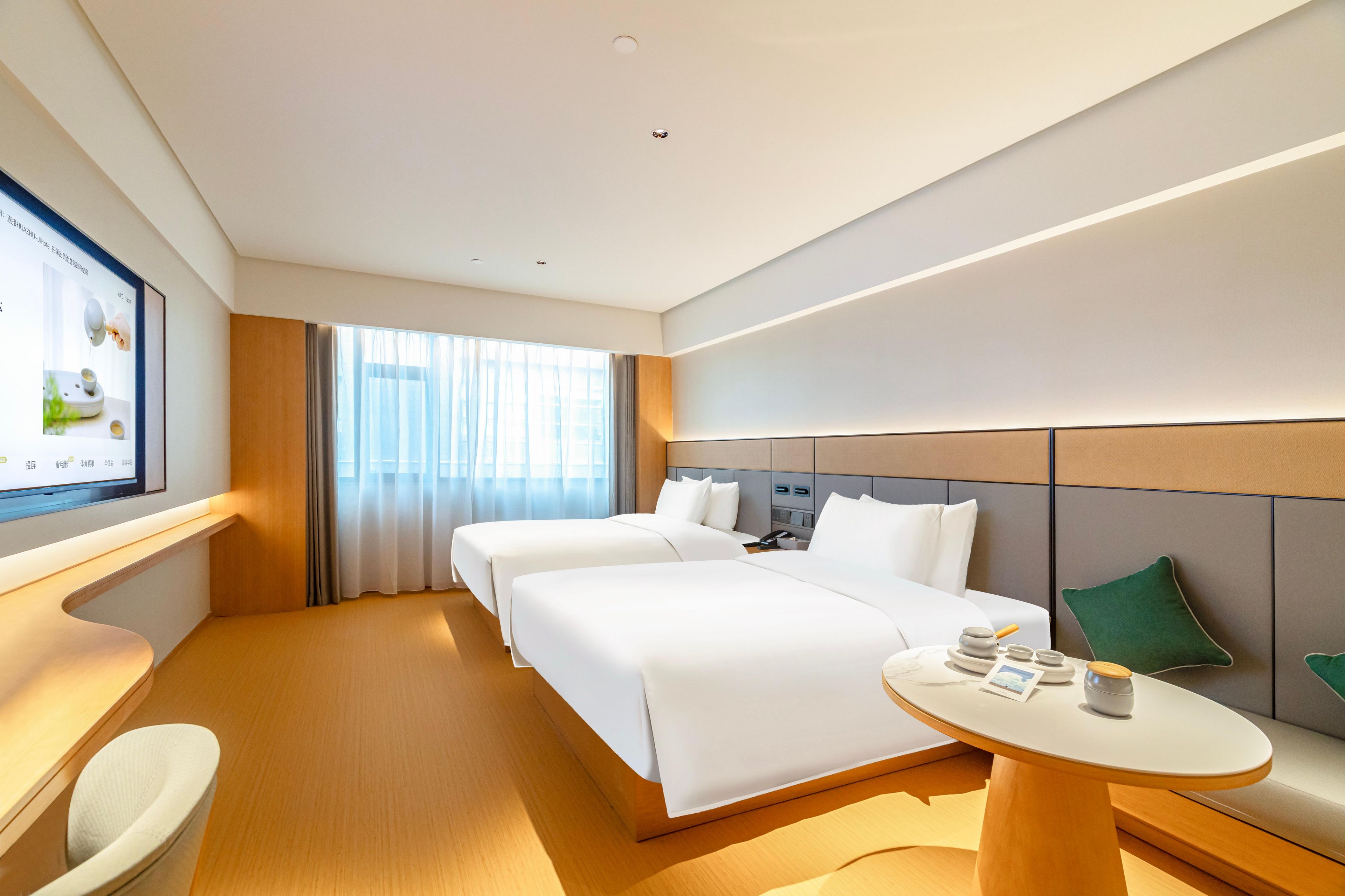 Ein Hotelzimmer mit zwei Betten, einem kleinen Tisch und einem Fernseher an der Wand.