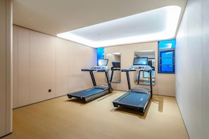Un gimnasio moderno con dos cintas de correr, un espejo grande y techo con iluminación azul.