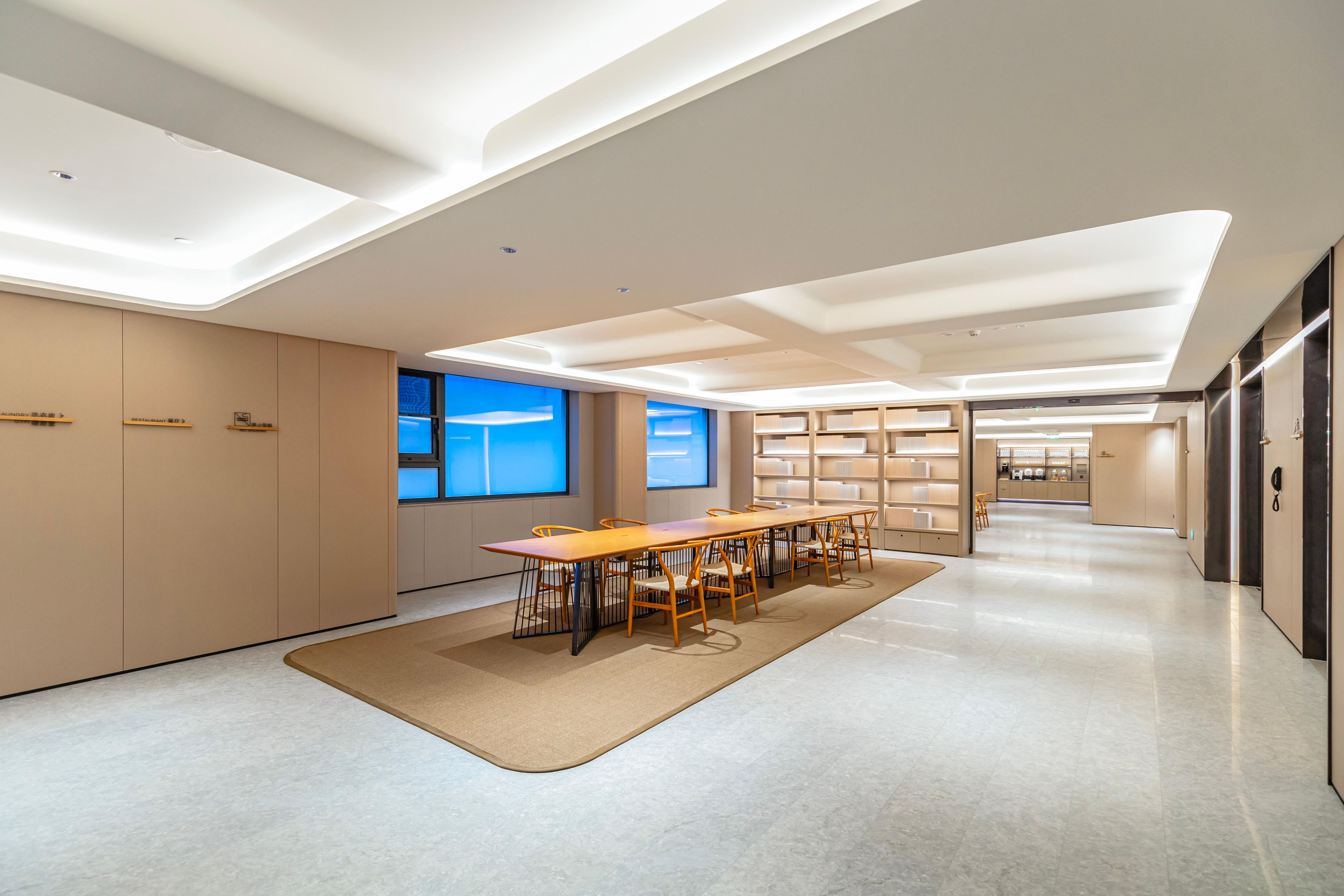 A modern conference room with a long table and chairs, a large window, and a bookshelf.