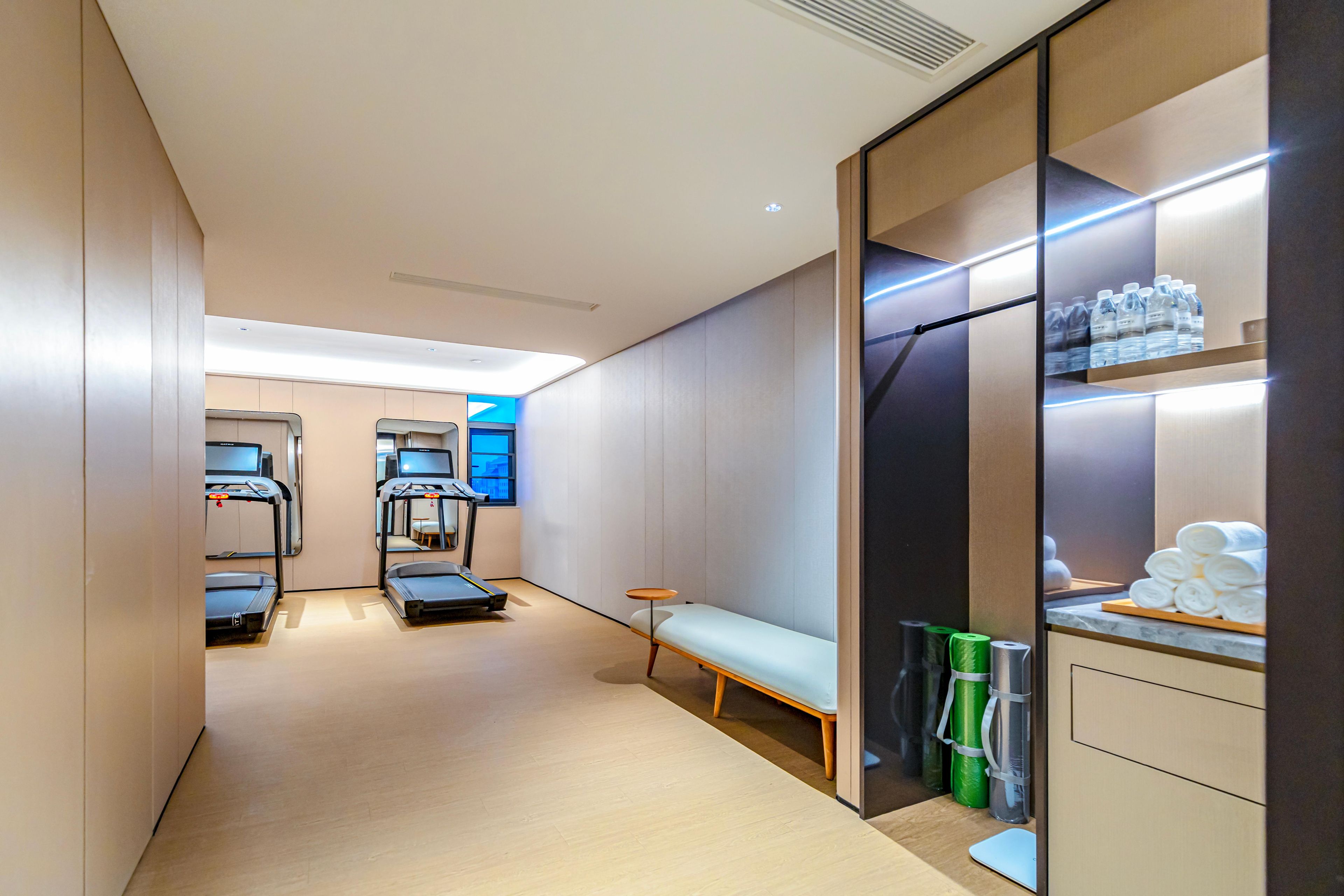 A hotel room with a treadmill, a bench, a small table, and a shelf with toiletries.