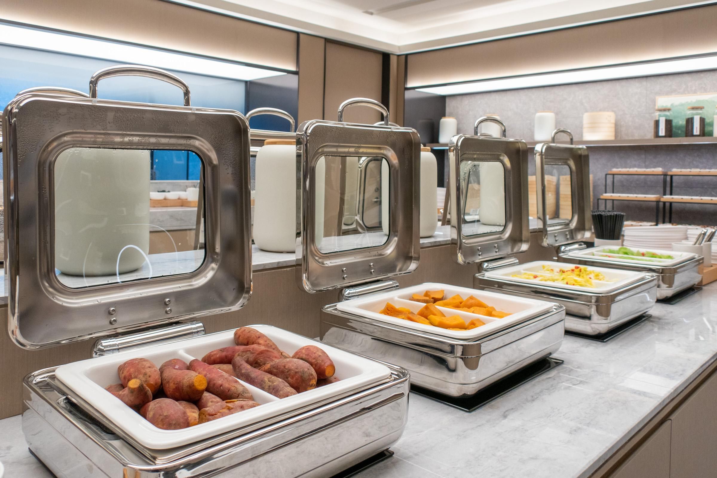 Een buffetopstelling met diverse etenswaren in metalen bakken, waaronder een hoek met zoete aardappelen.