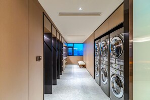 A hotel hallway with a row of washing machines on one side and a seating area with a view of the cityscape. - JI Hotel (Xi'an)