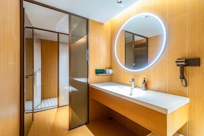 A modern bathroom with a glass shower door, a white sink, and a mirror with a circular light. - JI Hotel (Xi'an)