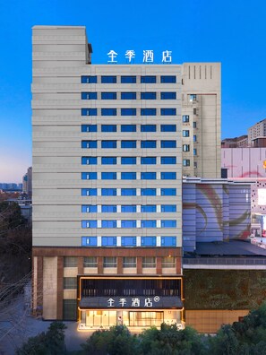 A multi-story hotel with a modern facade, large windows, and a ground-level entrance with illuminated signage. - JI Hotel (Xi'an)