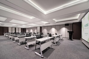 Uma sala de conferências com várias mesas e cadeiras, um púlpito e uma tela de projeção.