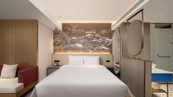 Una habitación de hotel moderna con una cama grande, un espacio de descanso con una silla roja, un televisor montado en la pared y un baño con espejo y lavamanos.