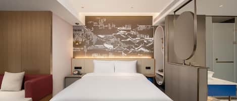 A modern hotel room with a large bed, a seating area with a red chair, a wall-mounted TV, and a bathroom with a mirror and sink.