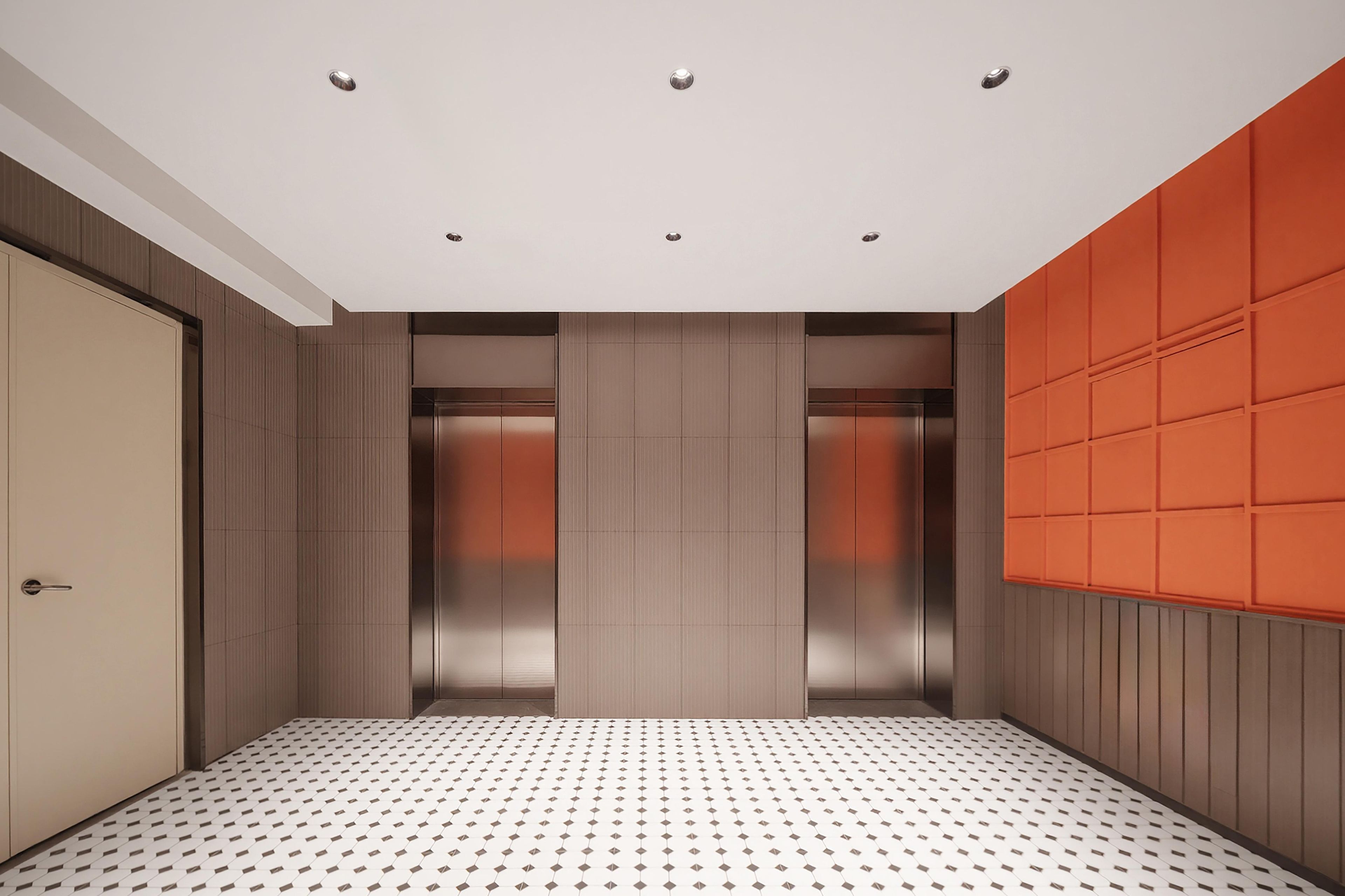 Interior de un ascensor con piso estampado, puertas metálicas y pared con diseño geométrico.