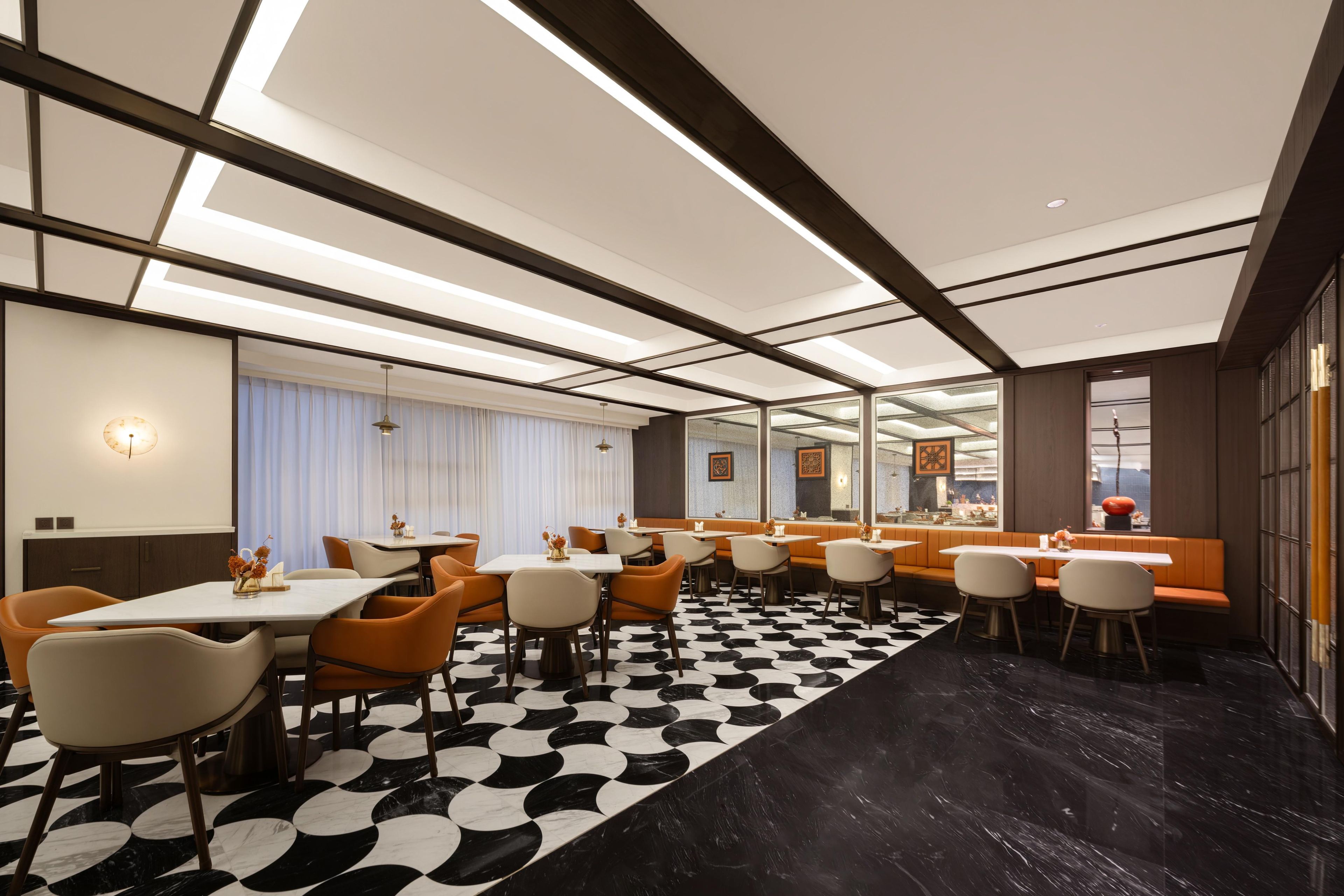 Un comedor de hotel moderno con suelo de diseño blanco y negro, varias mesas y sillas naranja.