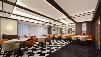 A modern hotel dining area with a black and white patterned floor, multiple dining tables, and orange chairs.