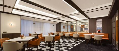 A modern hotel dining area with a black and white patterned floor, multiple dining tables, and orange chairs.