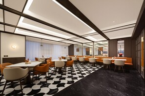 Ein moderner Hotel-Speisebereich mit einem schwarz-weißen Fußbodenmuster, mehreren Esstischen und orangefarbenen Stühlen.