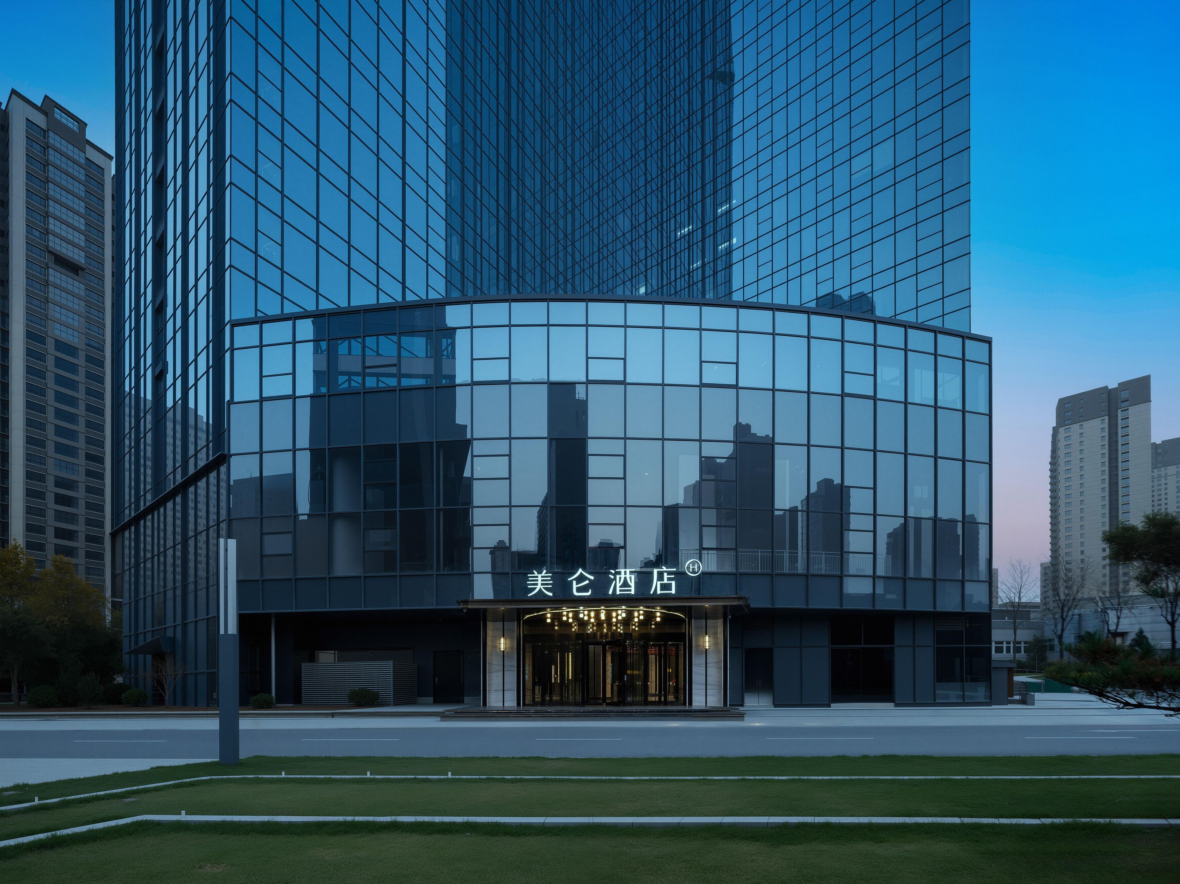 A modern hotel with a glass facade, a prominent entrance with a sign, and a well-maintained lawn in front.