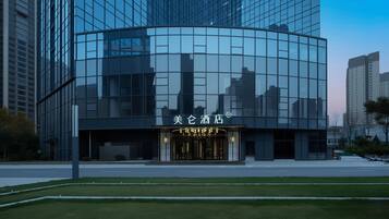 A modern hotel with a glass facade, a prominent entrance with a sign, and a well-maintained lawn in front.