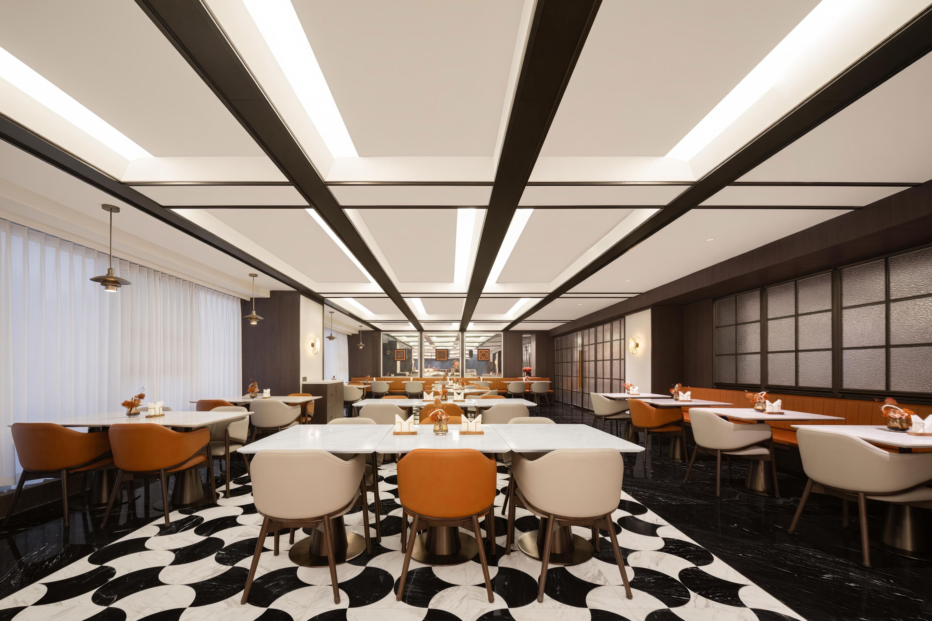 A modern restaurant with a long dining area, high ceilings, and a patterned floor.