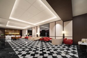 Eine moderne Hotelhalle mit Schachbrettmuster-Boden, Sitzbereichen und einer Rezeption.