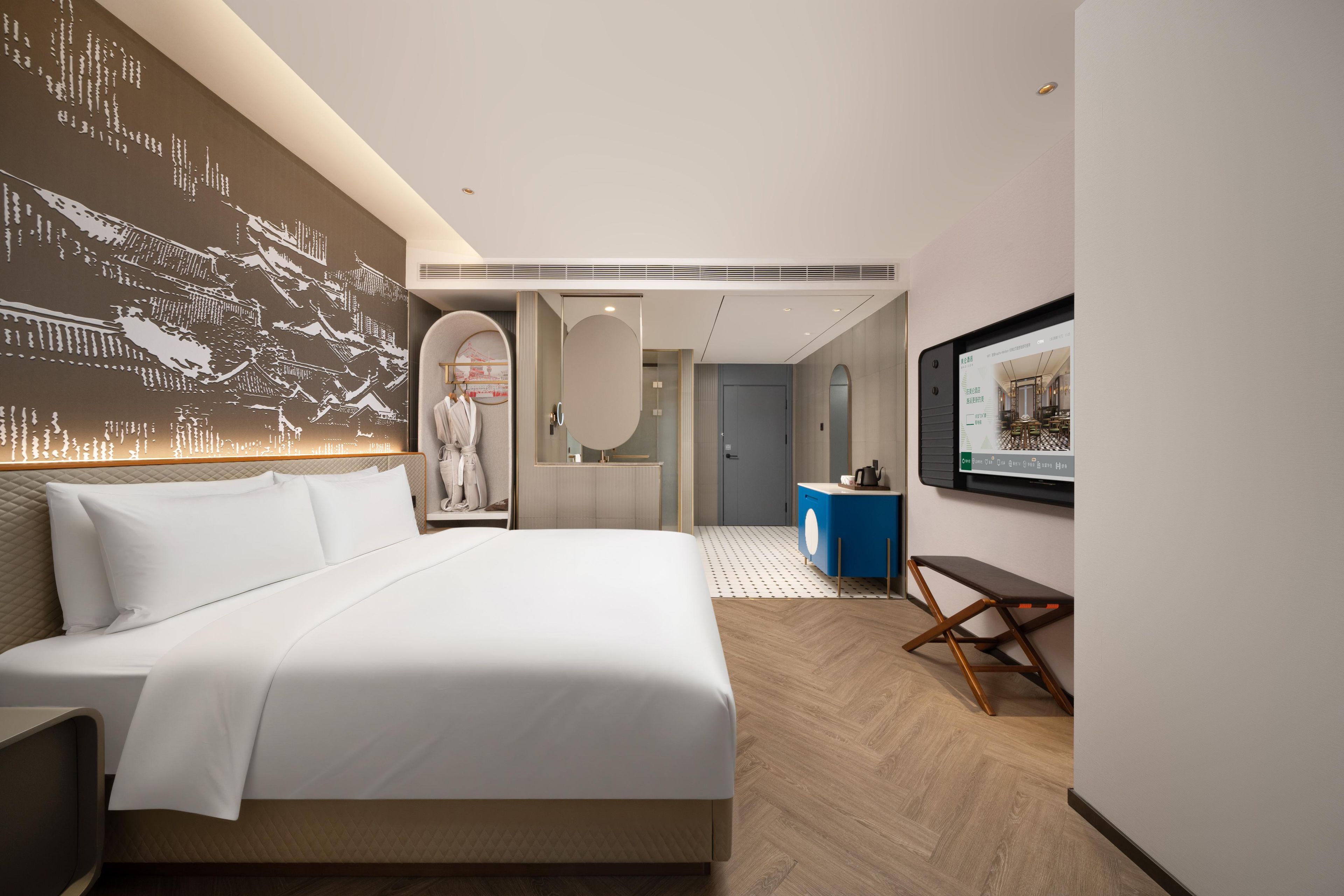 A modern hotel room with a large bed, a bathroom with a mirror, and a wall-mounted television.