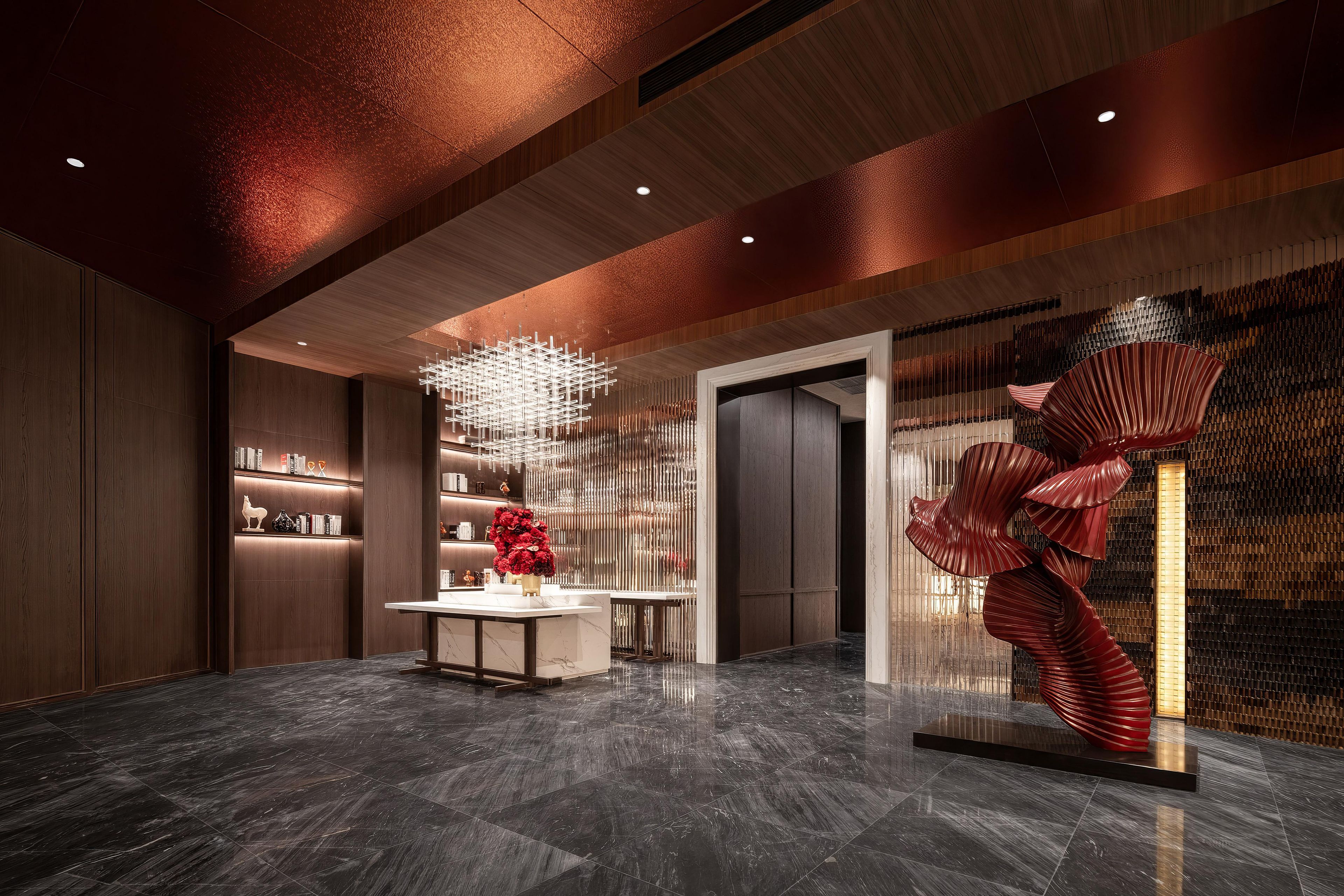 Un vestíbulo moderno con piso de mármol, un mostrador de recepción central y una escultura roja única.