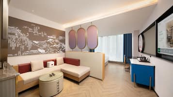A modern hotel room with a sofa, a small round table, a decorative wall piece, and a television.