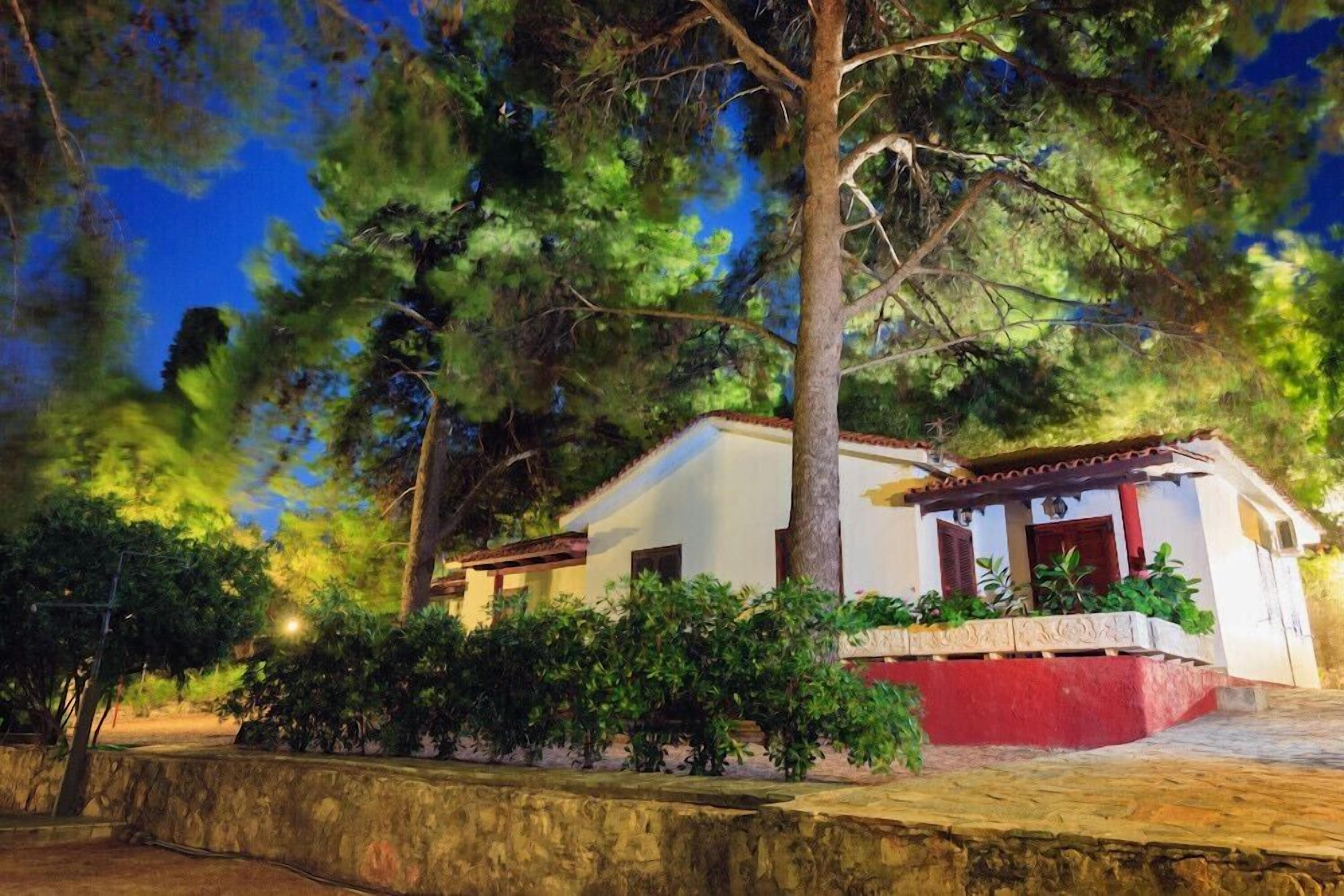 A white building with a red base, surrounded by trees and a stone wall.