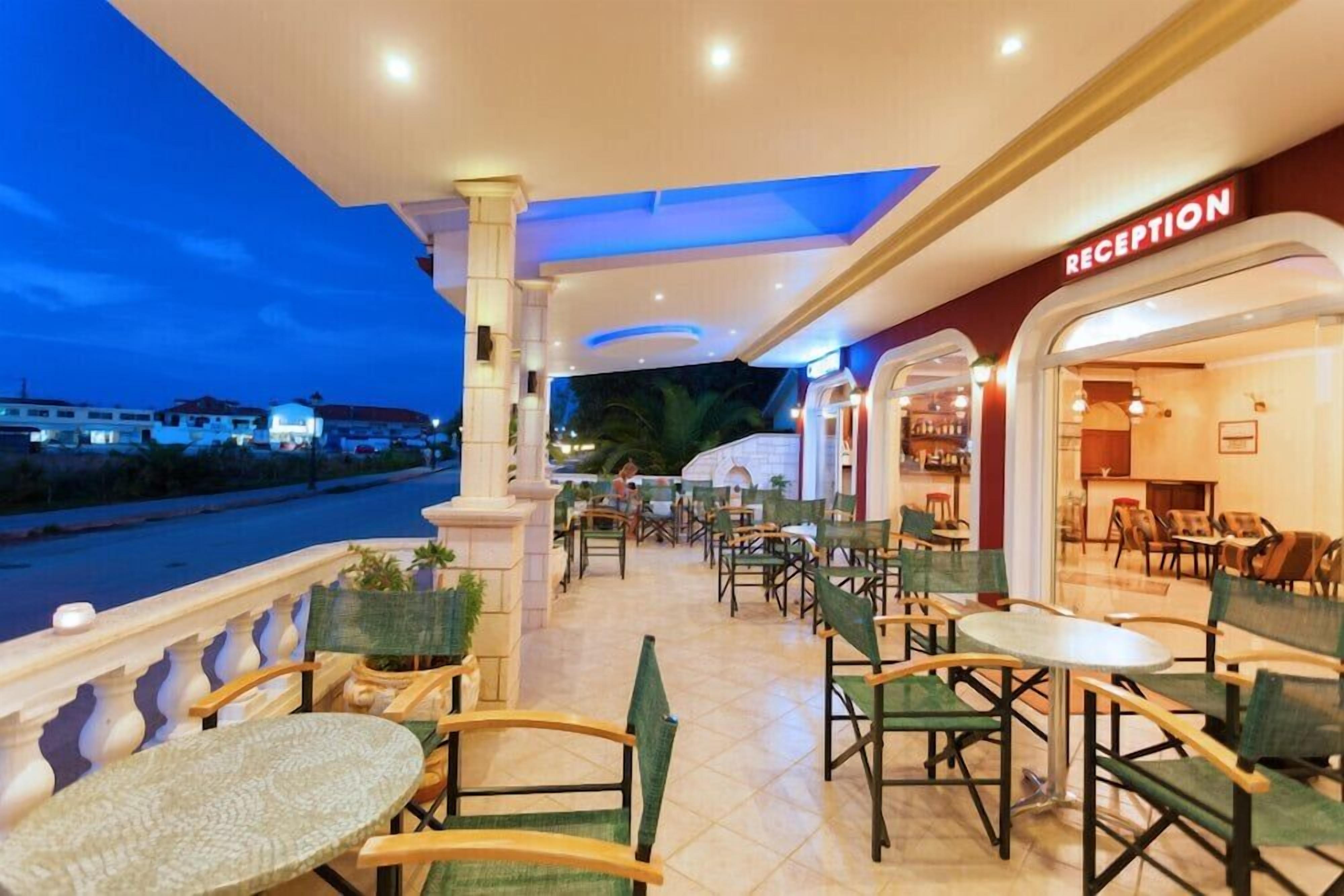 A hotel reception area with a view of the sea, outdoor seating with tables and chairs, and a reception desk.