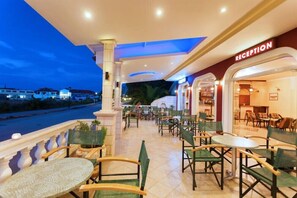 Zona de recepción de un hotel con vistas al mar, mobiliario exterior con mesas y sillas, y mostrador de recepción.