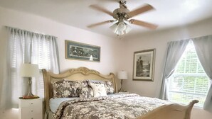 A bedroom with a bed, a ceiling fan, a nightstand, a lamp, and two framed pictures on the wall. - Pura Vida Biloxi (Biloxi)