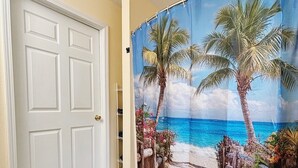 A room with a white door, a blue shower curtain depicting a beach scene, and a dark blue rug. - Pura Vida Biloxi (Biloxi)