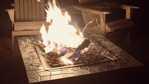 A fire pit with burning logs, surrounded by Adirondack chairs. - Pura Vida Biloxi (Biloxi)