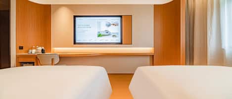A hotel room with two beds, a desk with a computer, and a large screen displaying a hotel website.