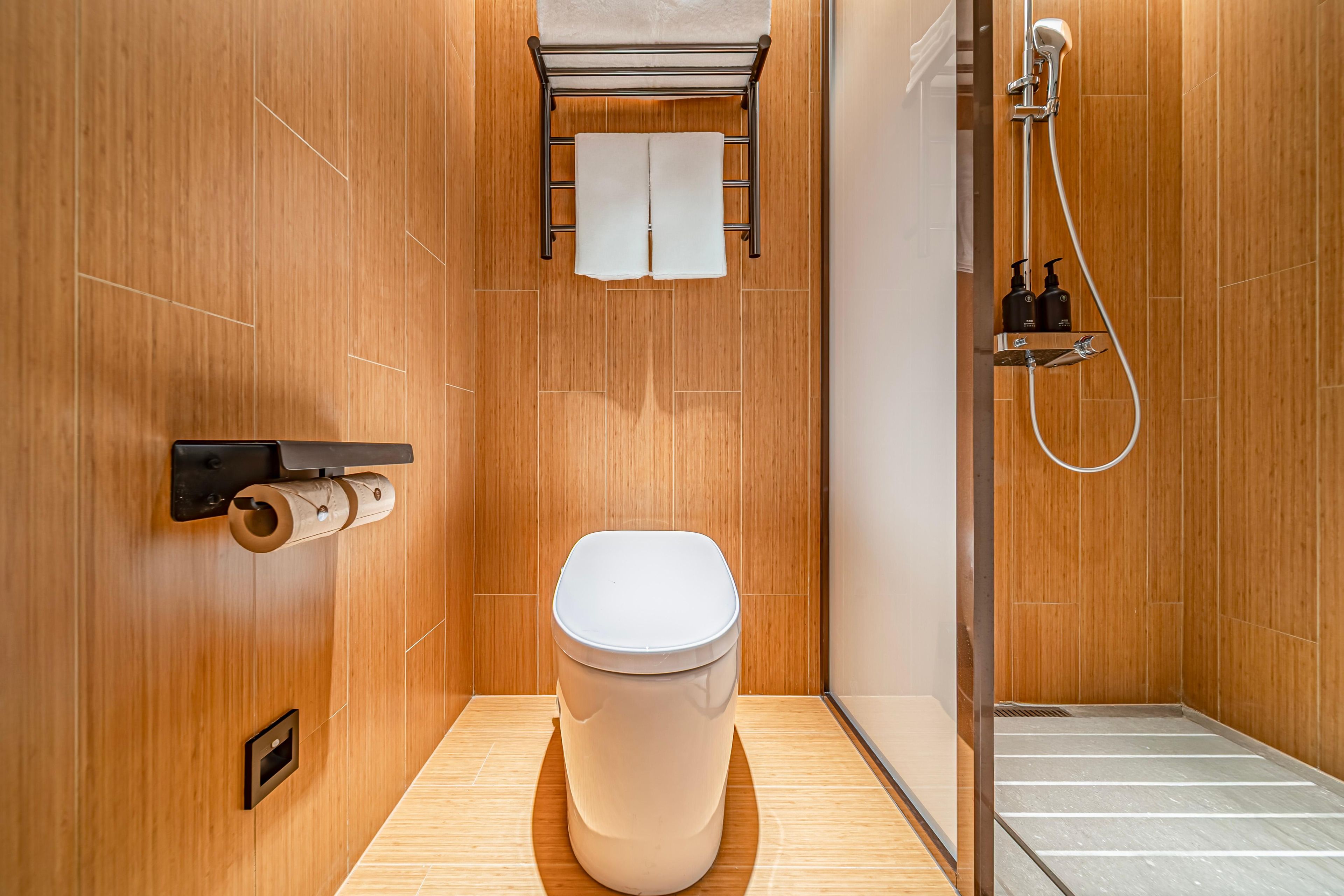A modern bathroom with a toilet, a towel rack, a shower, and a toilet paper holder.