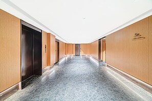 A modern hallway with wooden paneling and a marble floor, leading to a door with a digital elevator control panel. - JI Hotel (Xi'an)