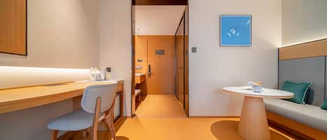 Une chambre d’hôtel moderne avec un bureau en bois, une chaise, une table ronde et un canapé agrémenté d’un coussin.