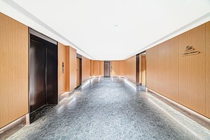 En moderne gang med træpaneler og et marmorgulv, der fører til en dør med et digitalt elevatorkontrolpanel.