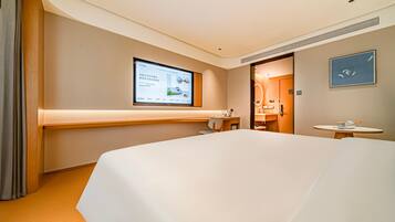 Habitación de hotel con una cama grande, un escritorio, una silla, una mesita, una pantalla de televisión y la puerta del baño.