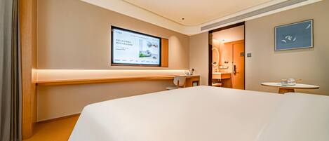 Une chambre d’hôtel avec un grand lit, un bureau, une chaise, une petite table, un écran de télévision et une porte de salle de bain.