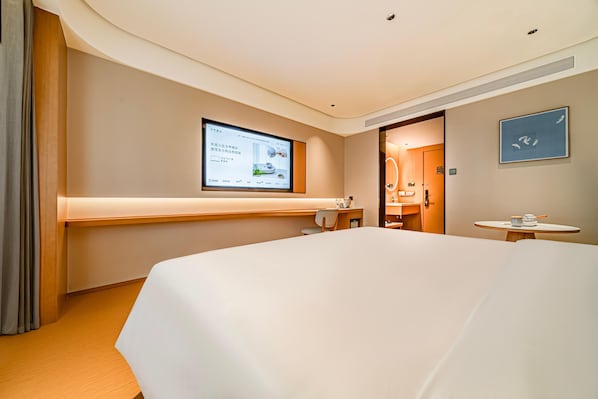 A hotel room with a large bed, a desk, a chair, a small table, a TV screen, and a bathroom door. - JI Hotel (Xi'an)