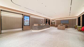 A modern hotel lobby with a reception desk, seating area, and a large digital screen.
