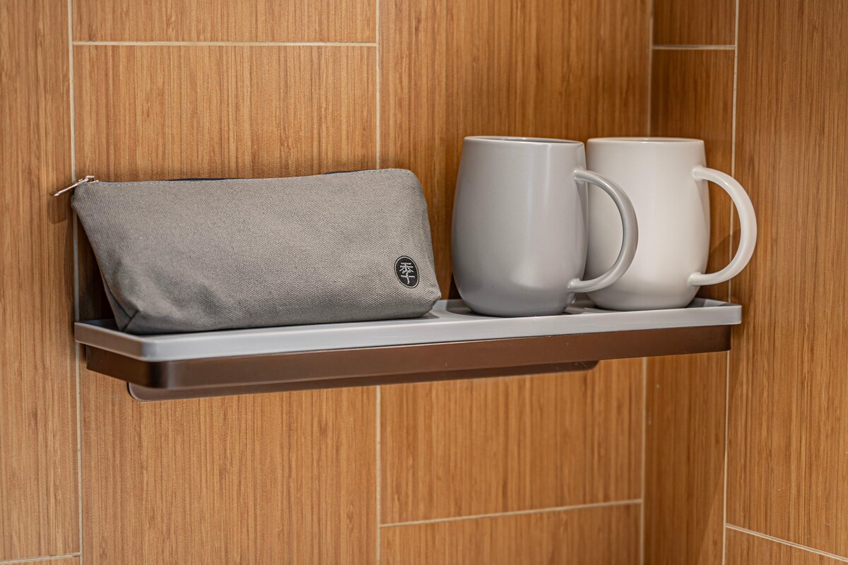 Una pared de madera con un estante que sostiene una bolsa gris y dos tazas blancas.