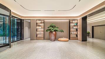 Een moderne lobby met een grote kamerplant, boekenkasten en een marmeren vloer.