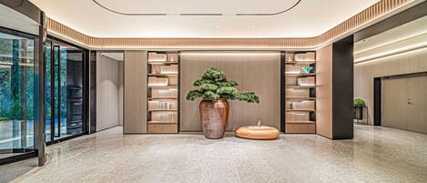 A modern lobby with a large potted plant, bookshelves, and a marble floor.