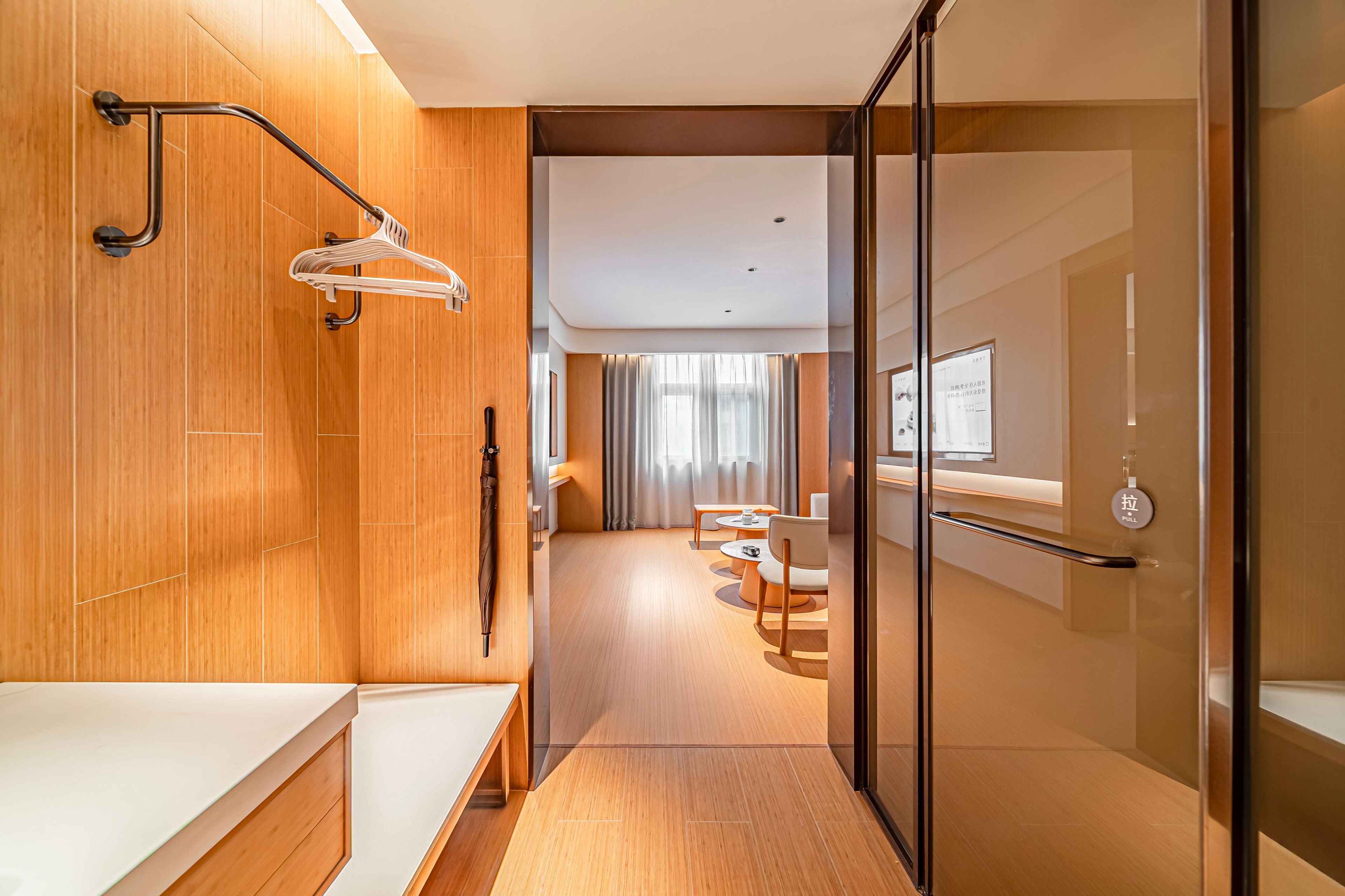 Una habitación de hotel moderna con suelo de madera, cabina de ducha de vidrio, tocador de madera y una zona de estar con una mesa y sillas.