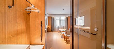 Una habitación de hotel moderna con suelo de madera, cabina de ducha de vidrio, tocador de madera y una zona de estar con una mesa y sillas.