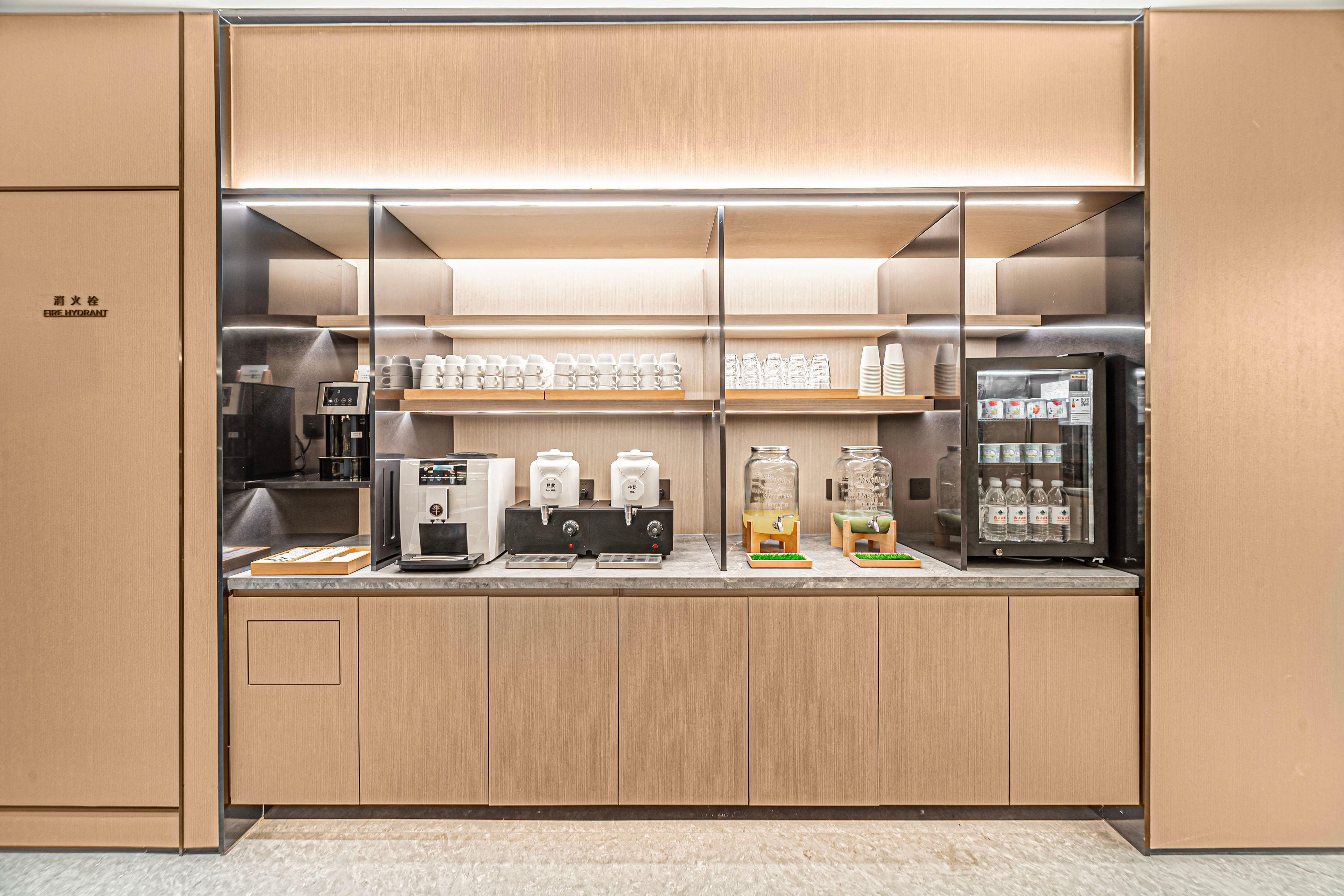 A modern kitchenette with built-in appliances, including a coffee machine, tea dispensers, and a refrigerator.