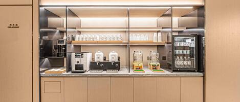 A modern kitchenette with built-in appliances, including a coffee machine, tea dispensers, and a refrigerator.