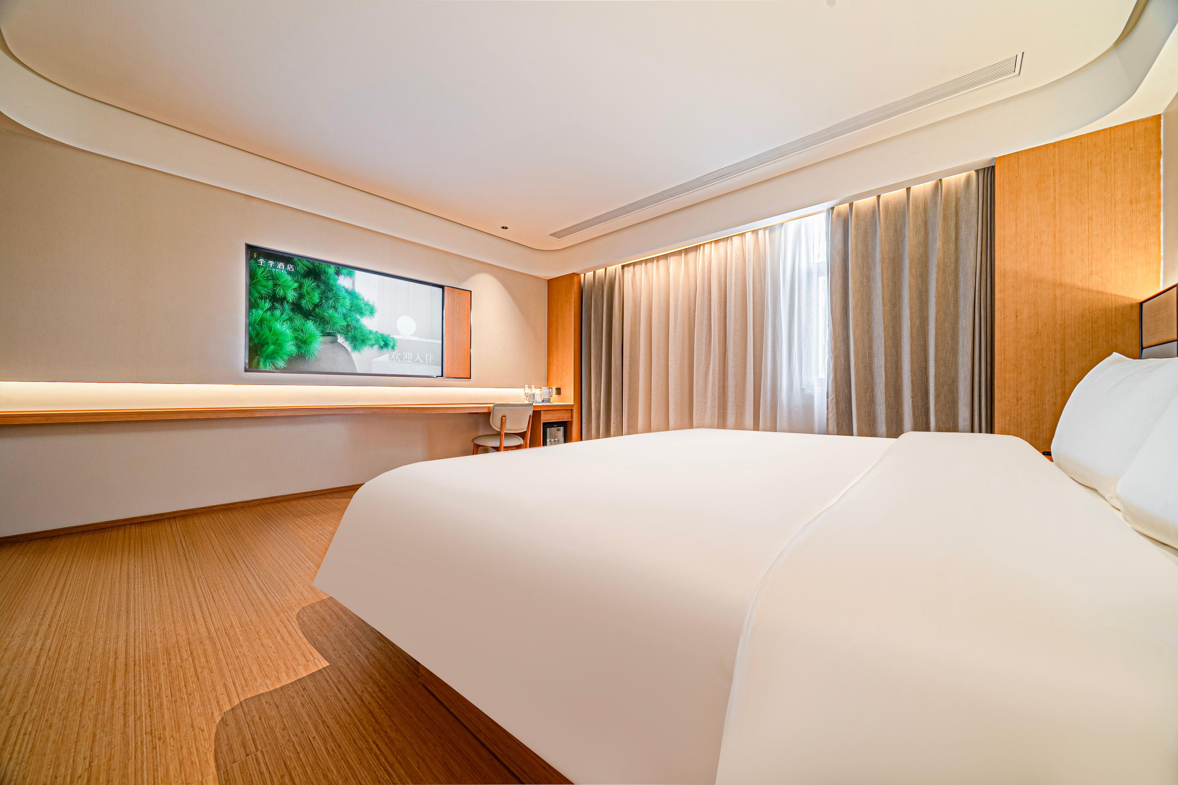 A hotel room with a large bed, a desk, a chair, a television, and a window with curtains.