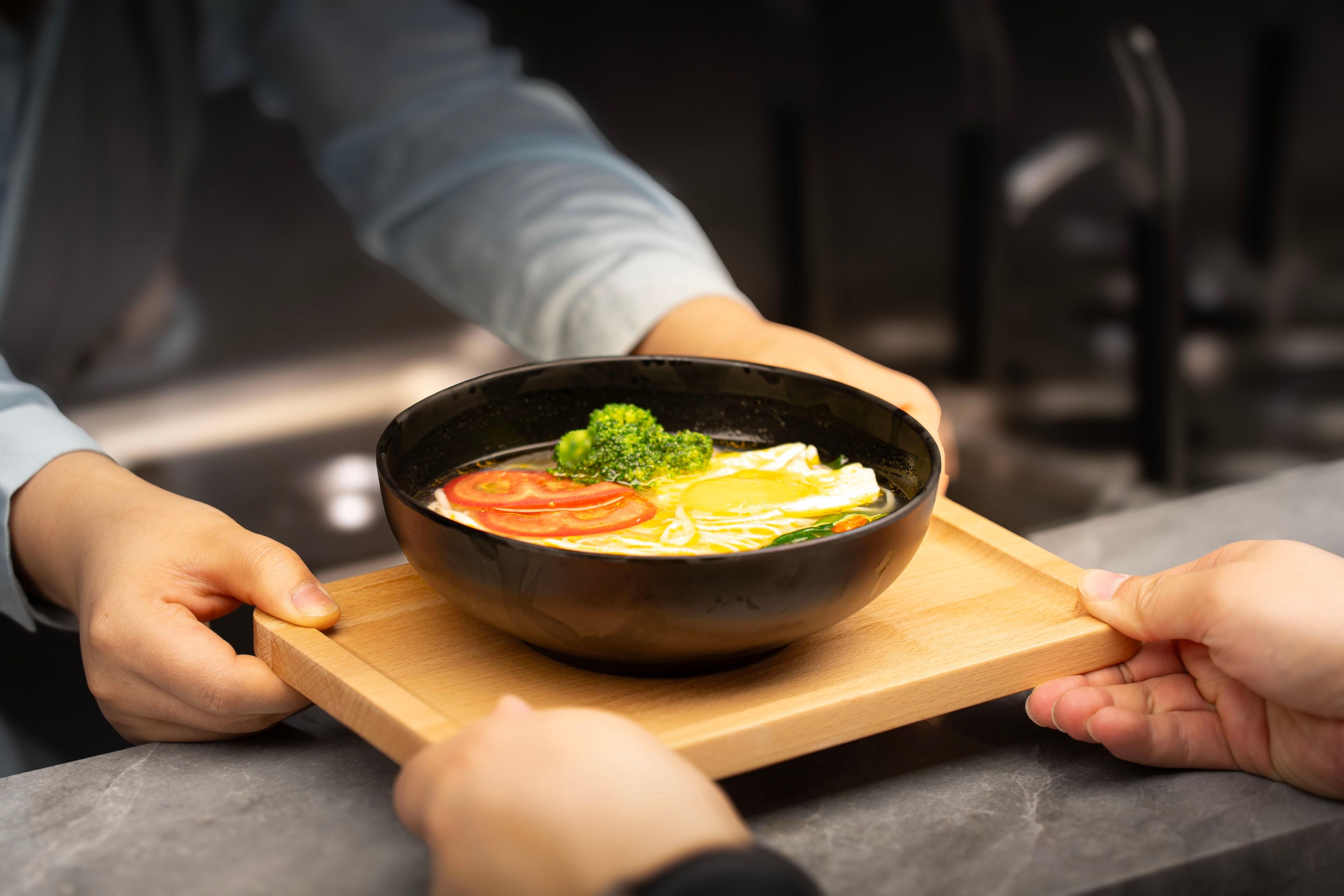 A person holding a bowl of soup on a wooden board.
