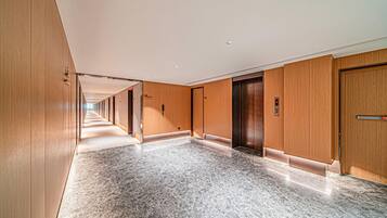 A long corridor with wooden paneling and marble flooring, leading to an elevator and a door.
