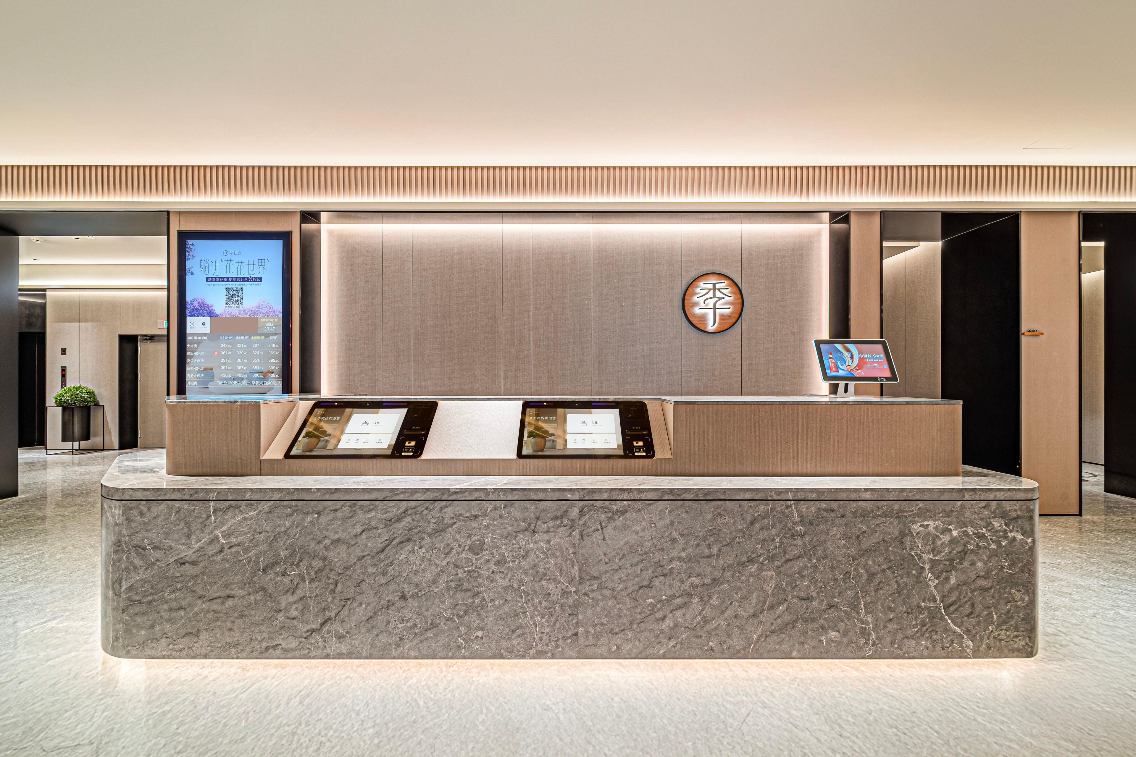 A reception desk with a digital display, a wooden panel with a logo, and a marble counter.