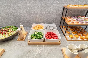 Noutopöytä, jossa on tarjolla monenlaista ruokaa, kuten salaatteja, hedelmiä ja leivonnaisia.
